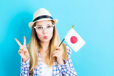 Happy young traveling woman holding Japanese flag